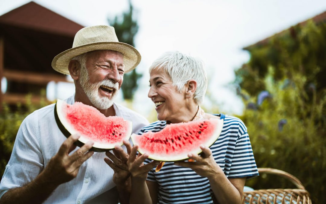 Cheerful senior couple having fun while eating watermelon in the backyard.